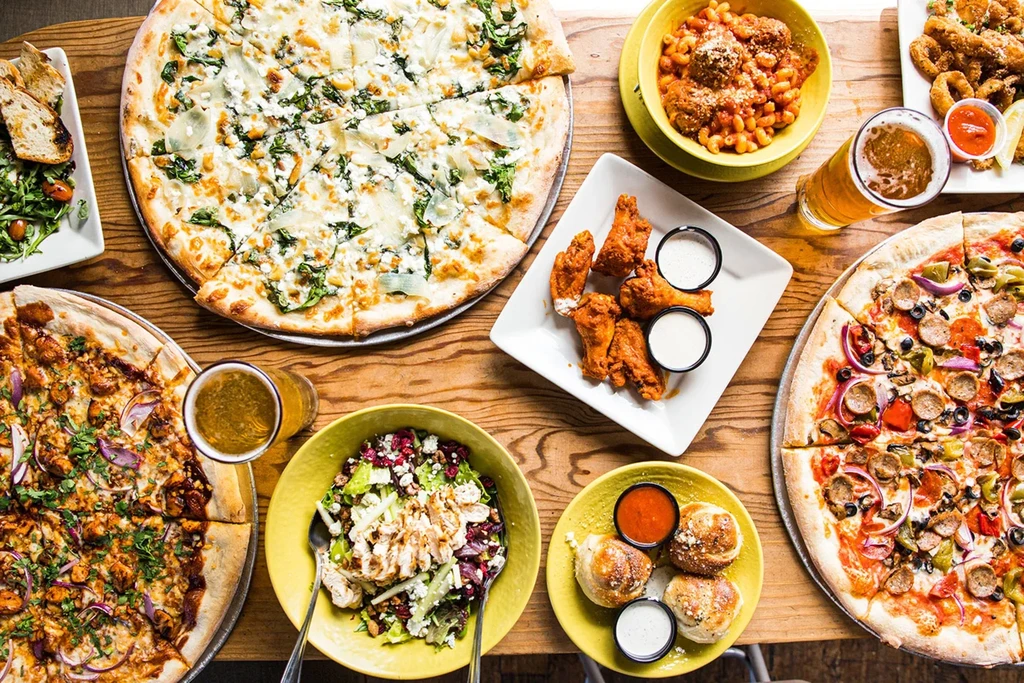 Overhead view of rustic table with pizzas, mac and cheese, wings, and beer.