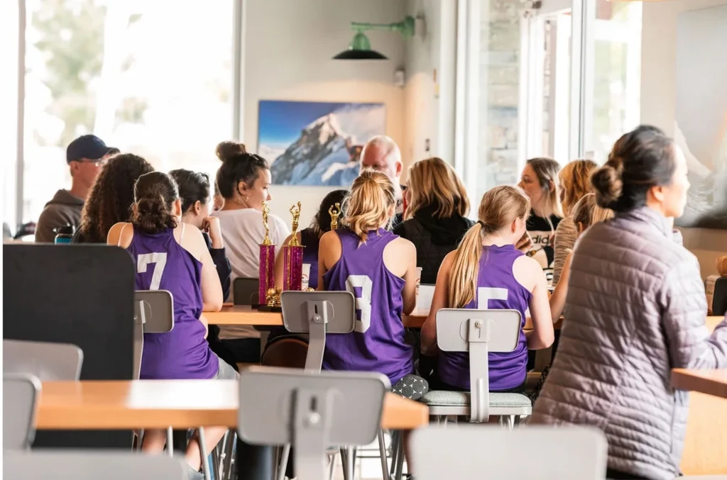 Group in purple jerseys with golden trophies at a cafe table.