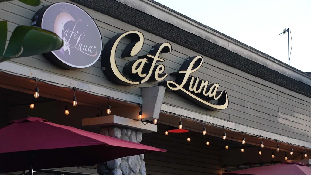 Illuminated Cafe Luna restaurant exterior with signs, warm lights, and umbrellas.