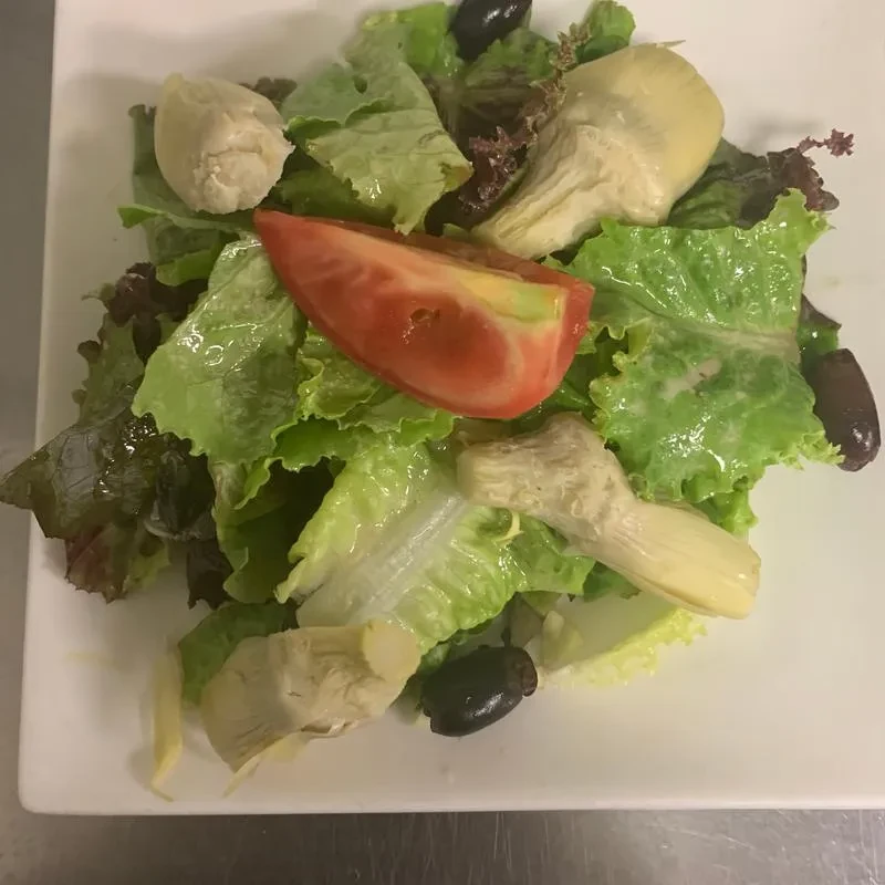 Fresh salad with lettuce, artichoke hearts, tomato, and olives.