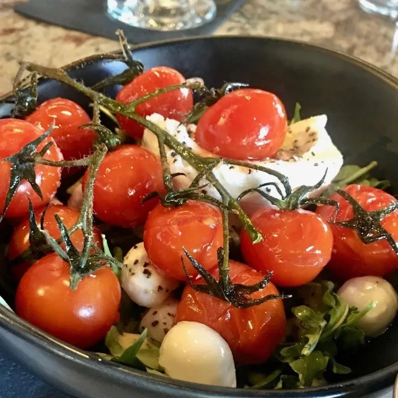 Close-up of roasted cherry tomatoes, mozzarella, and greens in a bowl.