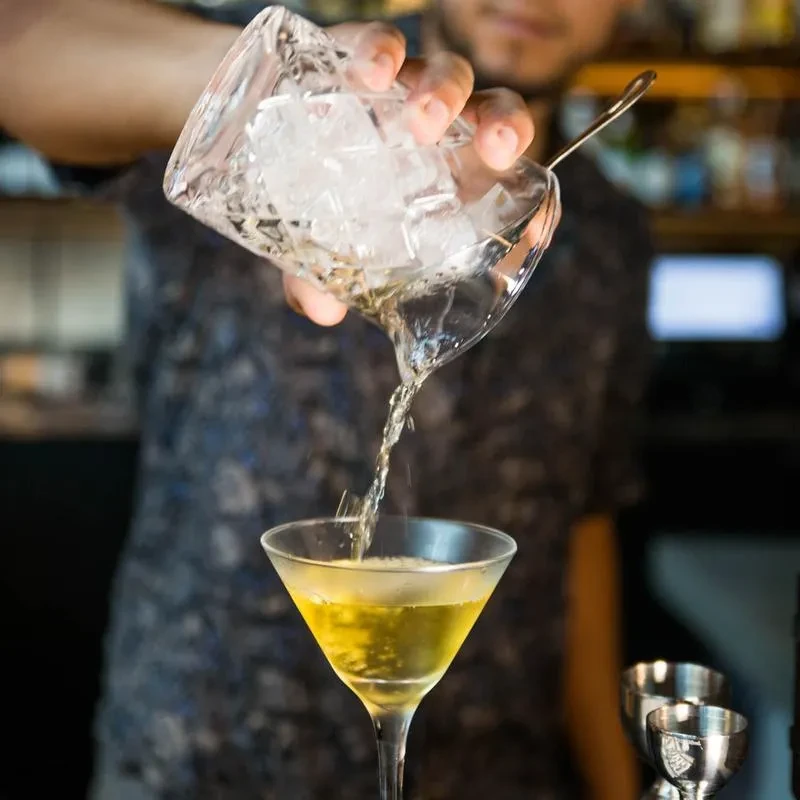 Hands pour iced cocktail from mixing glass into martini glass.