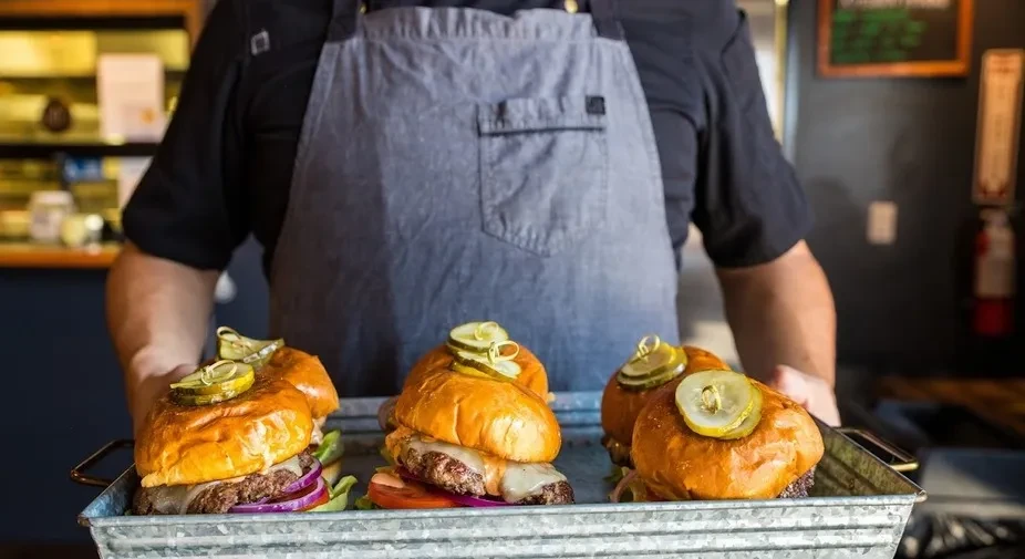 Chef holds metal tray of three gourmet cheeseburgers.