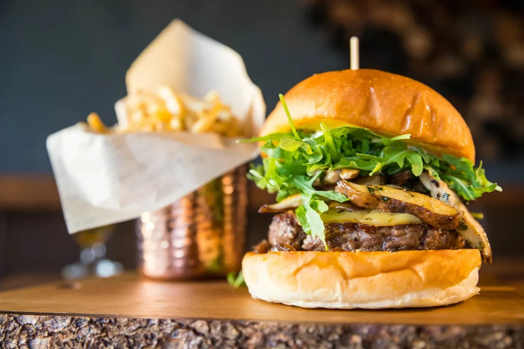 Burger with arugula and cheese, with fries on a wooden board.