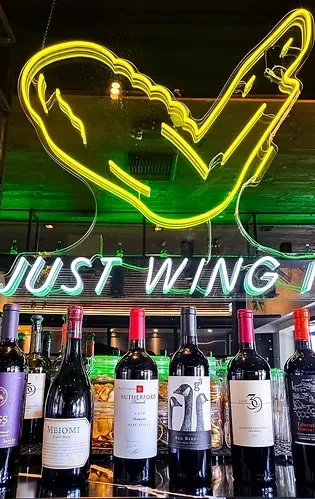 Six wine bottles below winged heart and 'JUST WING IT' neon.