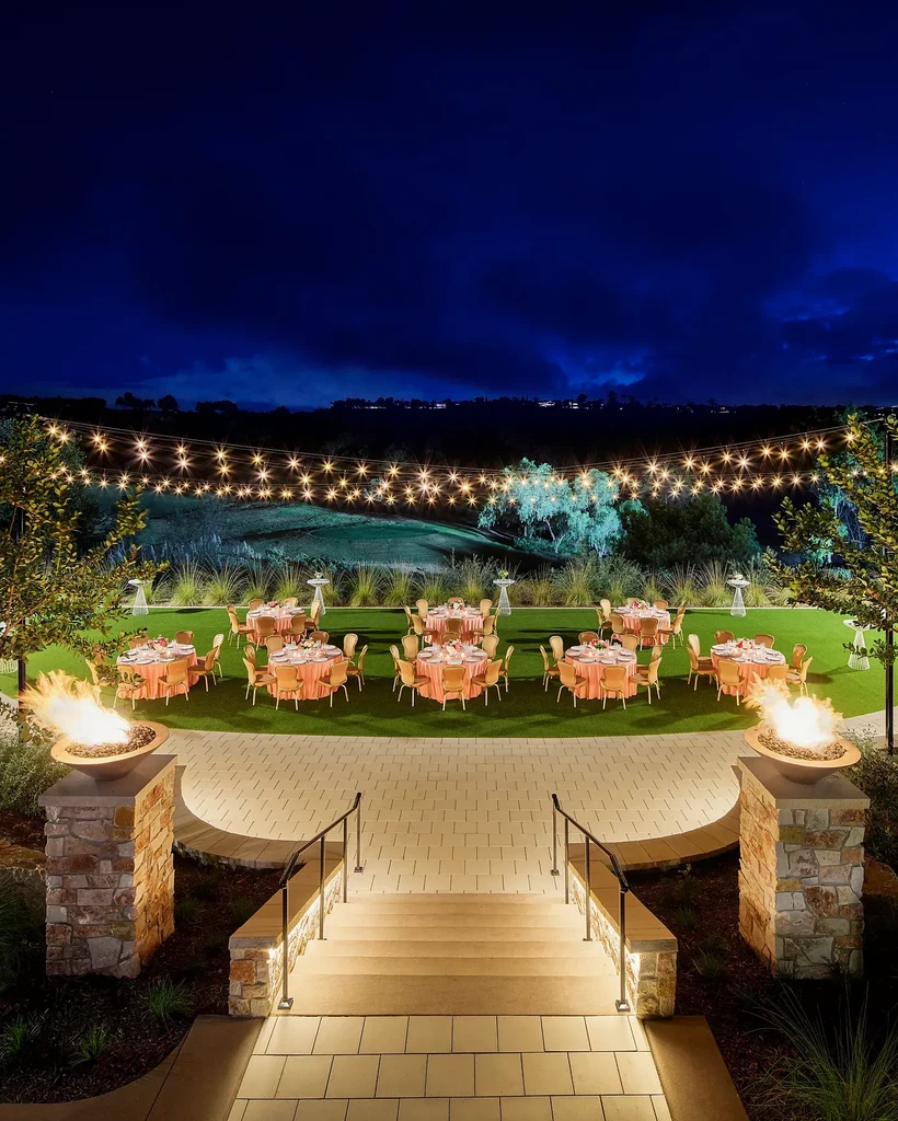 Nighttime outdoor dining area with fire pits, tables, and fairy lights.