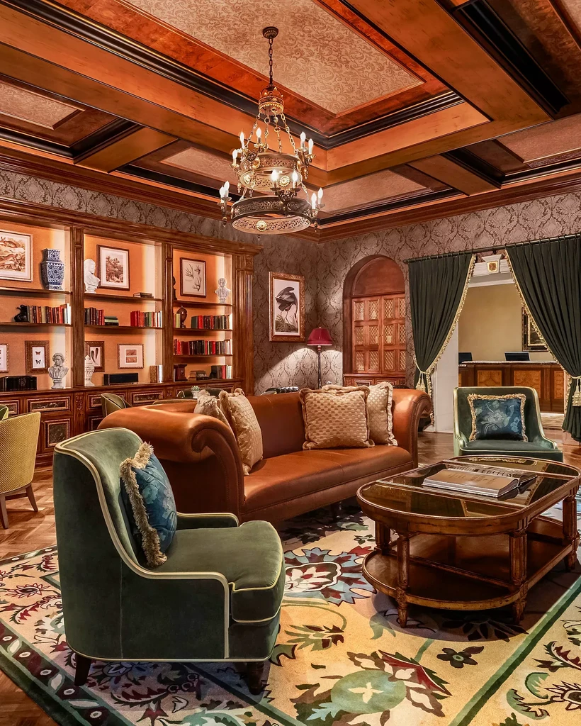 Opulent lounge interior featuring a chandelier, sofa, armchair, and bookshelf.
