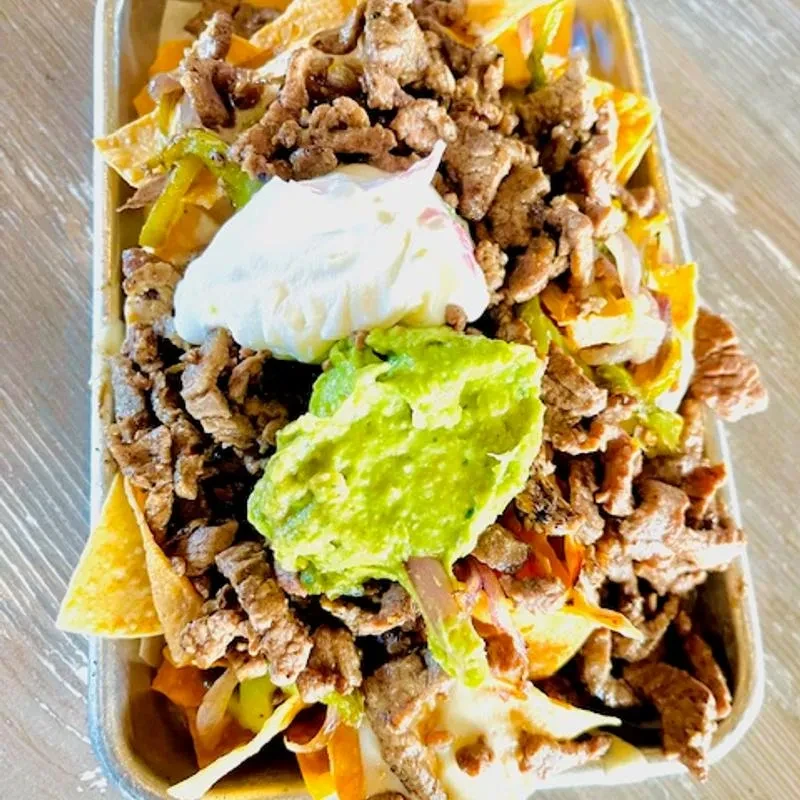 Loaded nachos in a metal tray with cheese, meat, sour cream, guacamole.