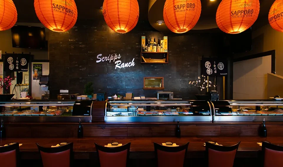 Japanese sushi bar interior with fresh fish display, red stools, and lanterns.