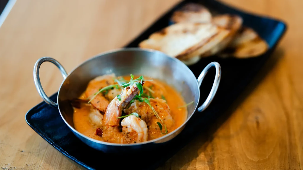 Shrimp in a stainless steel bowl with reddish-orange sauce and herbs.