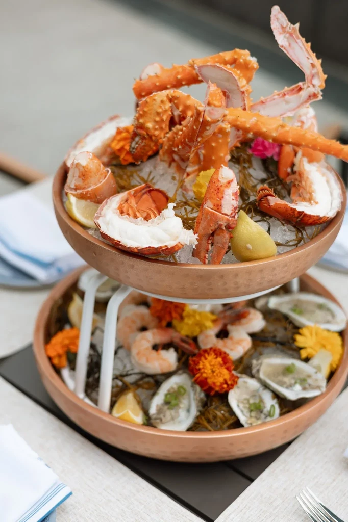 Two-tiered seafood tower with crab, lobster, shrimp, and oysters on ice.