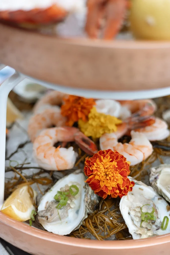 Tiered seafood platter with shrimp, oysters, lemon, and marigold flowers.