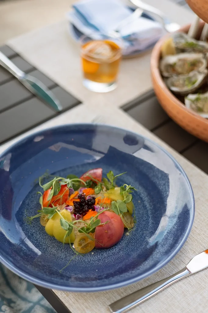 Colorful heirloom tomato and berry salad on a speckled blue ceramic plate.