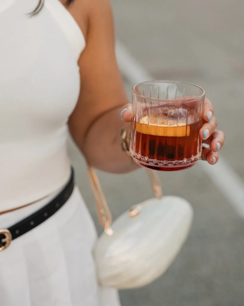 Close-up: Hand with blue nails holds a ridged glass of garnished cocktail.