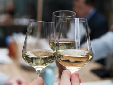 Three hands clinking white wine glasses in a toast.