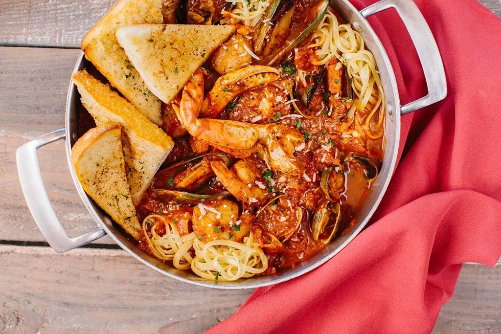 Seafood pasta in pan with crab, shrimp, mussels, clams, garlic bread.