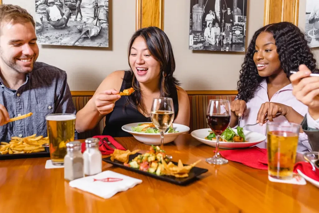 Three diverse diners laugh and eat a meal in a restaurant.