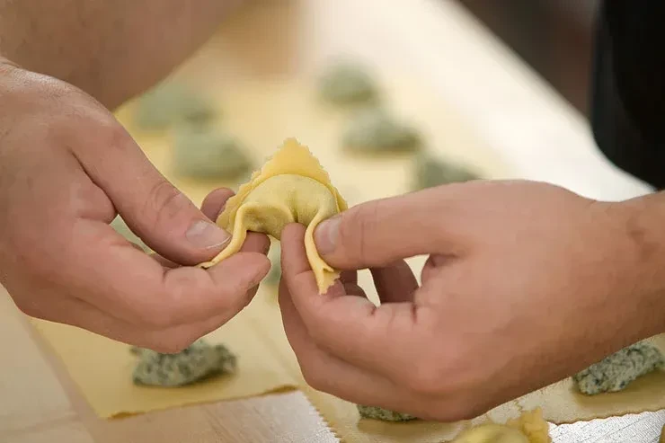 Two hands shaping fresh yellow pasta filled with green.
