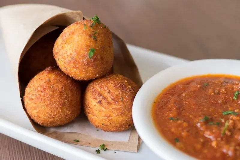 Three golden-brown breaded spheres in a cone with red sauce.