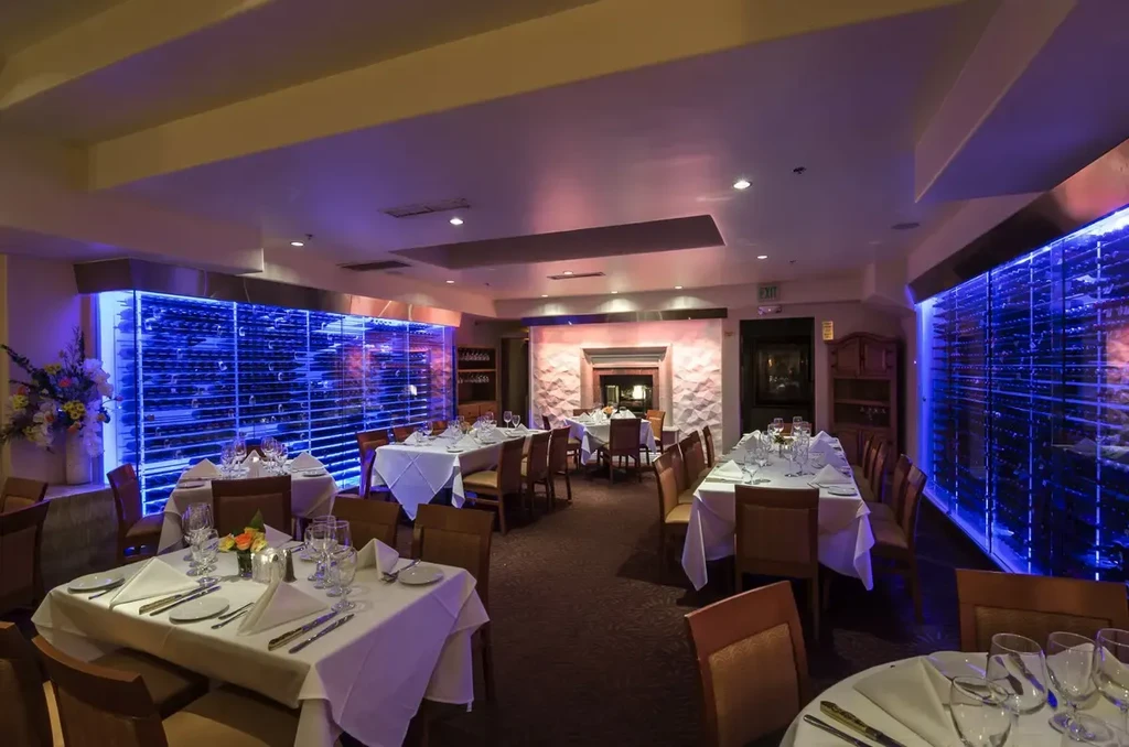 Dining room with set tables, blue LED wine walls, and fireplace.