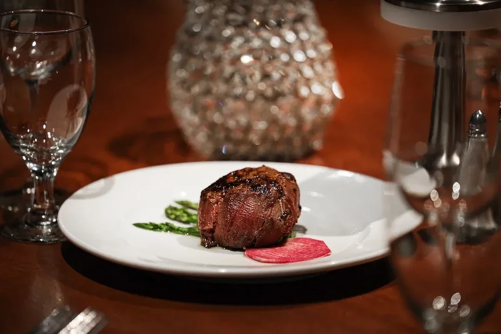 Medium-rare filet mignon steak with asparagus and a red vegetable slice.