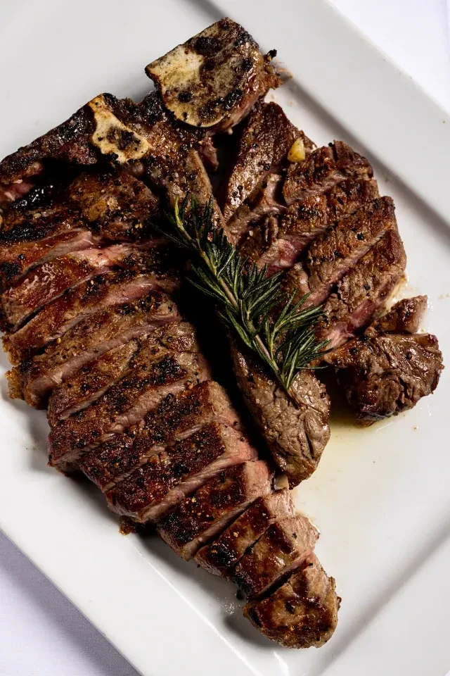 Medium-rare, sliced grilled T-bone steak garnished with rosemary.