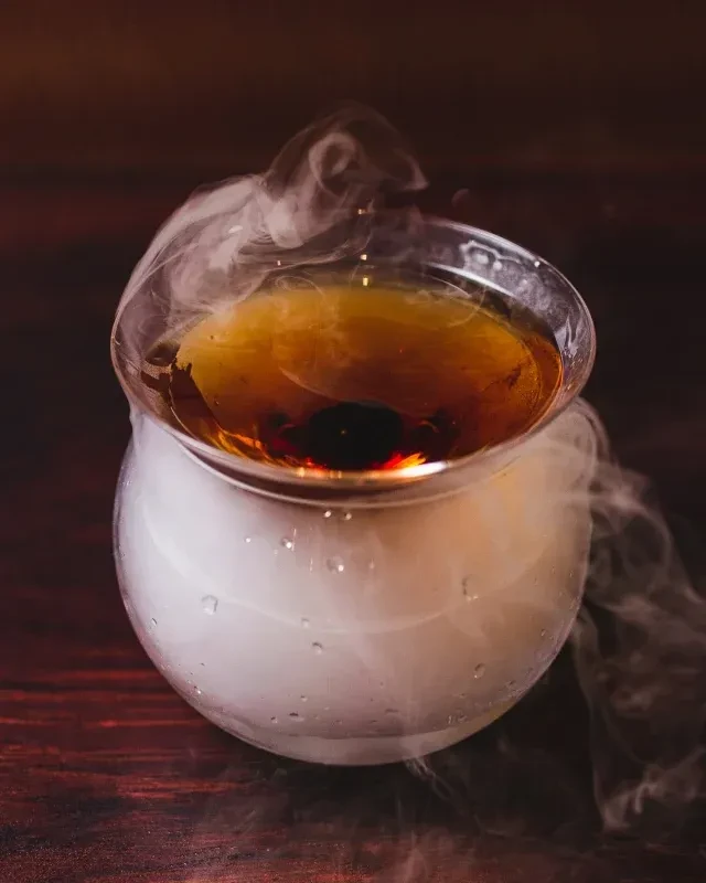 Amber cocktail in spherical glass with dramatic swirling smoke.