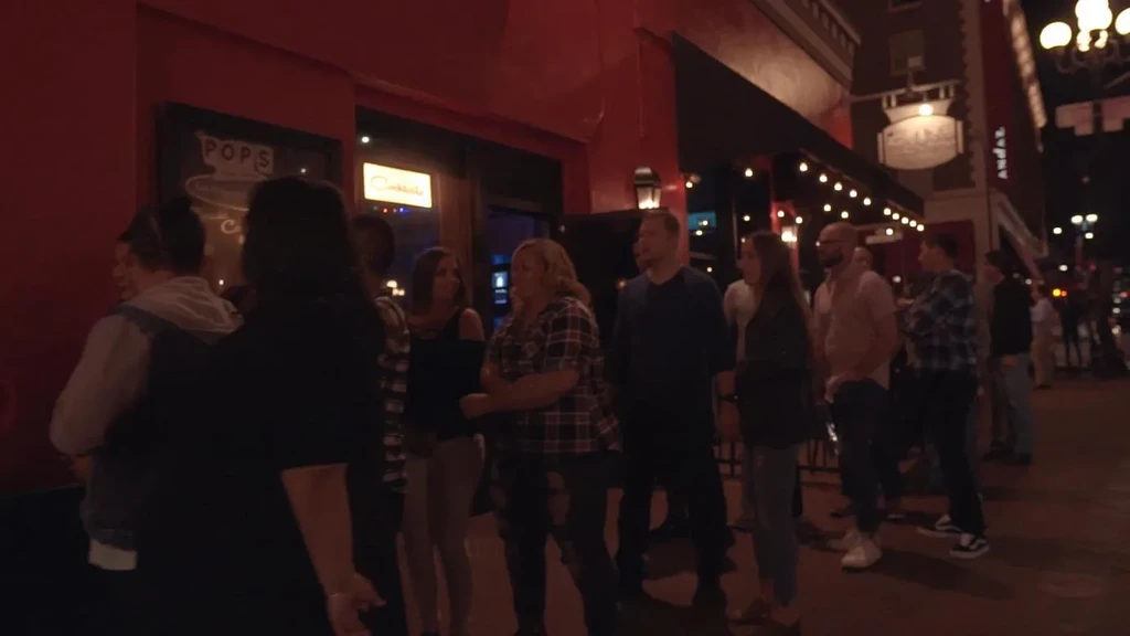People socializing outside a red bar with 'POPS' sign at night.