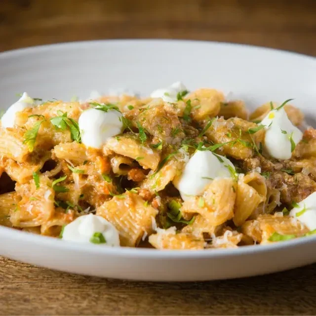Pasta in a bowl with reddish sauce, fresh herbs, and cheese.
