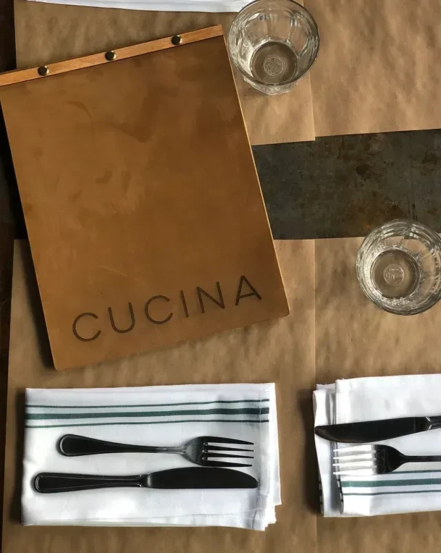 Flat lay of rustic CUCINA menu, silverware, and water glasses.