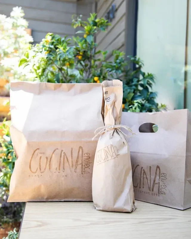 Three CUCINA enoteca branded takeout items on a wooden surface outdoors.