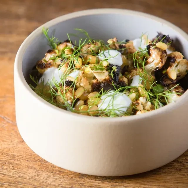 Top-down view of roasted cauliflower, herbs, pine nuts, and white sauce.