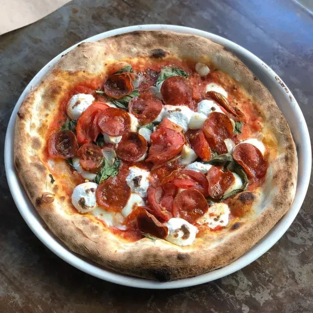 Charred round pepperoni pizza with mozzarella, basil, and tomatoes.