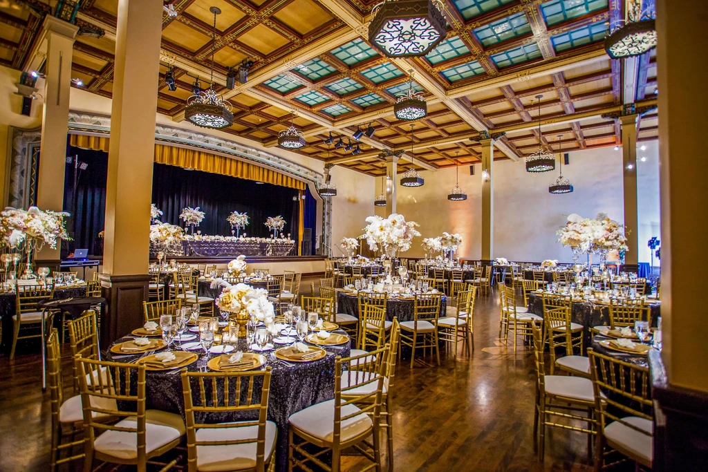 Formal event hall with round tables, floral centerpieces, and ornate chandeliers.