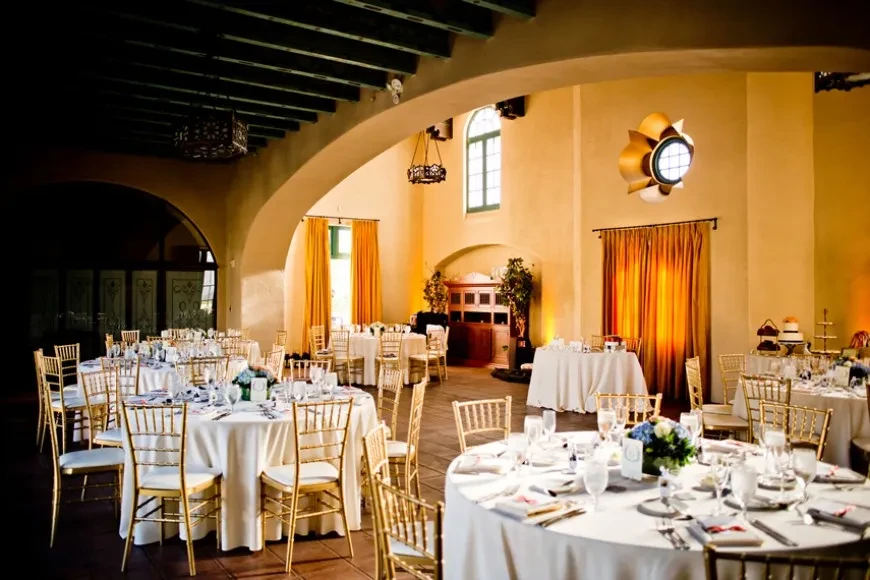 Elegantly set banquet hall with gold chairs and floral centerpieces.