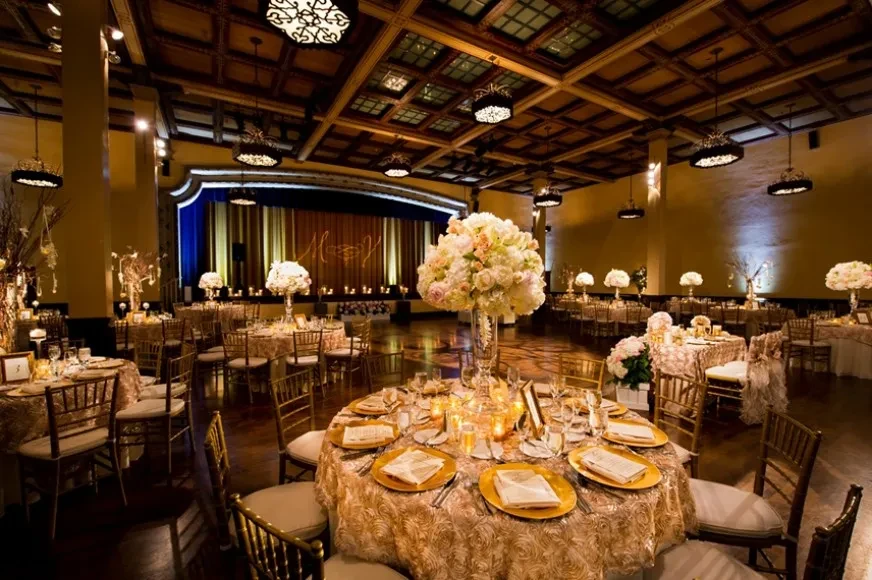 Luxuriously set ballroom with floral tables and a stage displaying initials.
