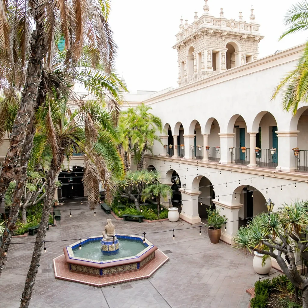 Spanish Colonial courtyard with octagonal tiled fountain, arcades, and string lights.