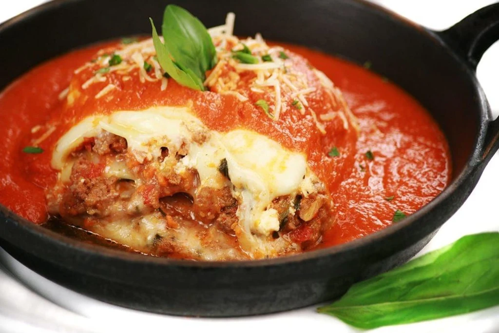 Skillet of Italian pasta with meat, cheese, red sauce, and basil.