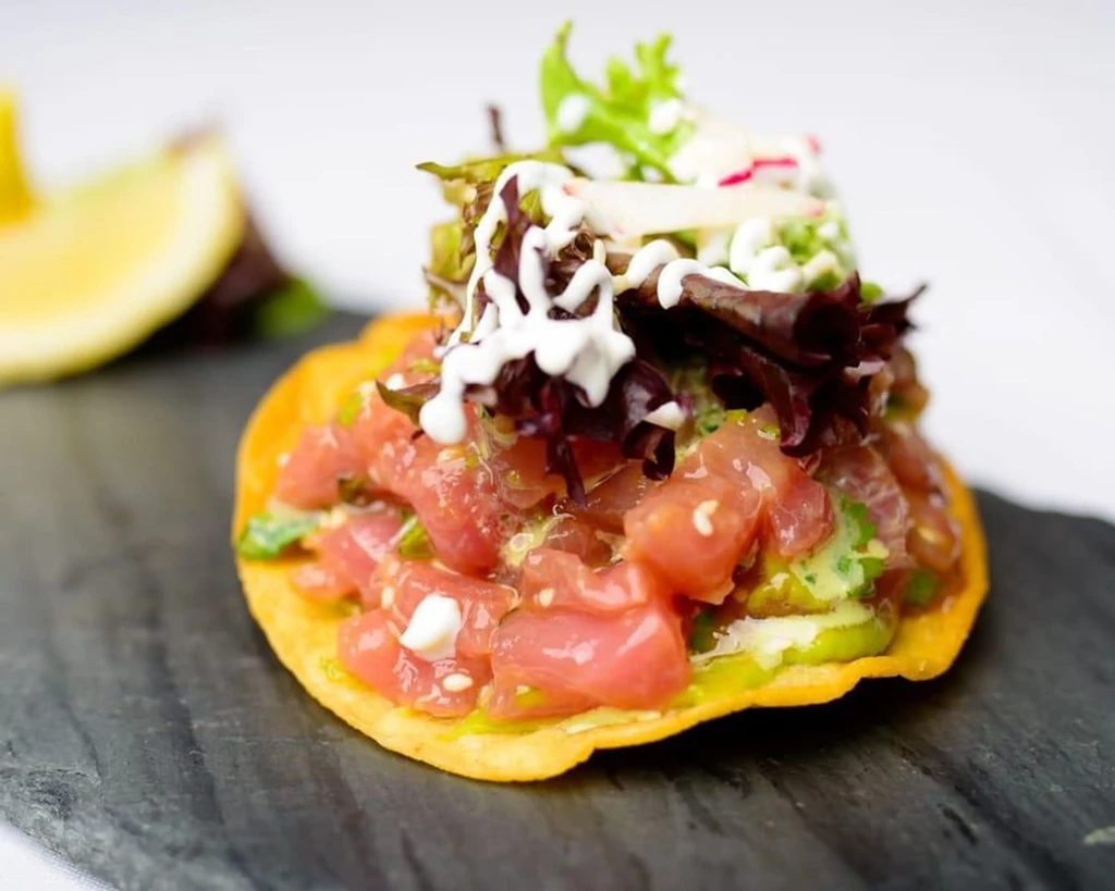 Crispy tuna poke tostada with avocado, greens, white sauce.