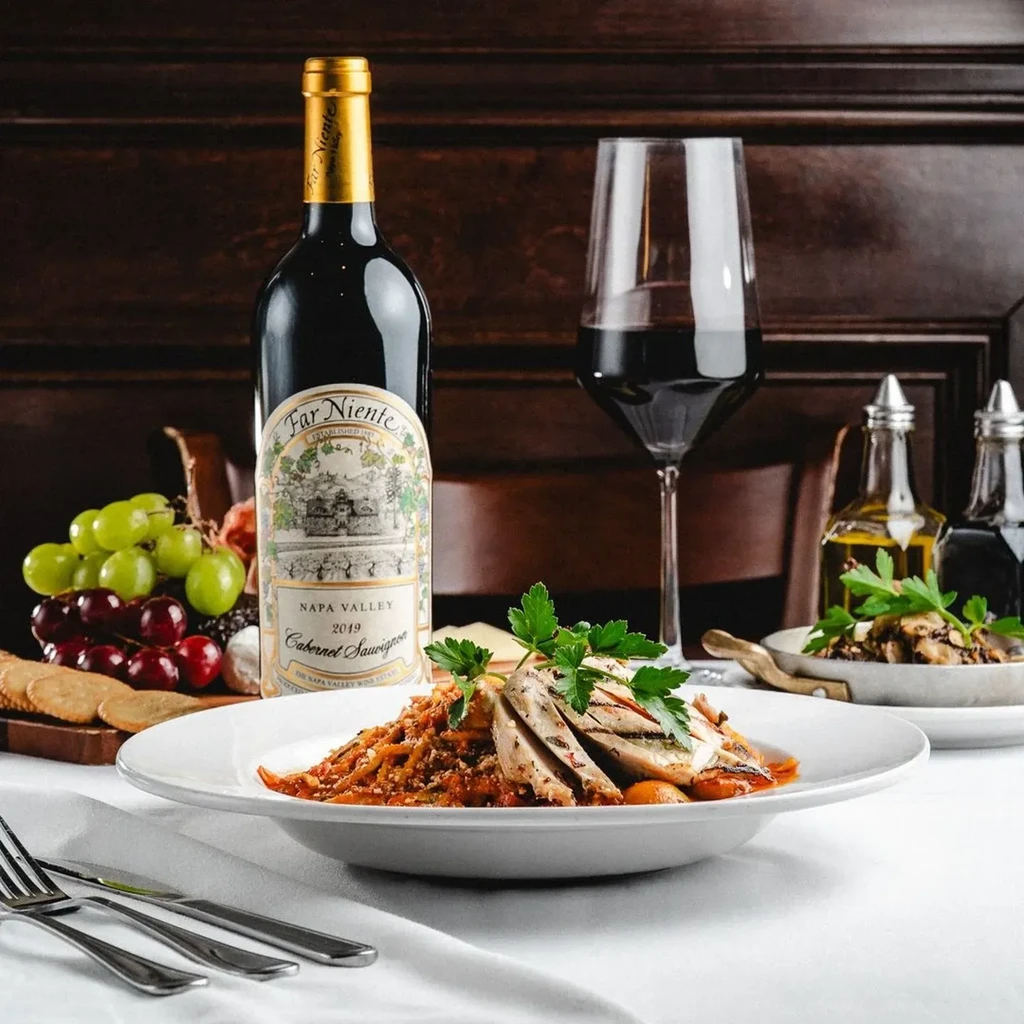 Grilled chicken, pasta, red wine, and cheese board on table.