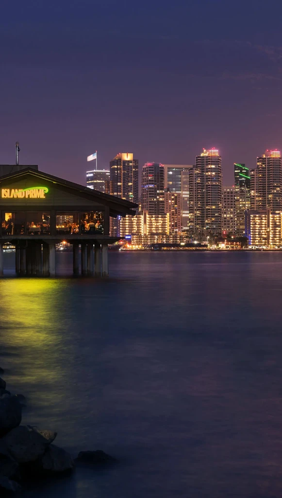 Island Prime restaurant, well-lit and reflecting on water, with city skyline.