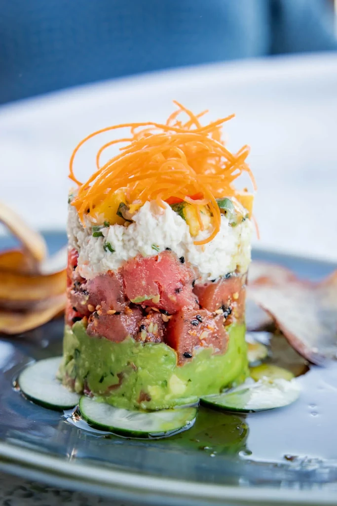 Layered tuna tartare stack with avocado, crab, carrots, and cucumber.