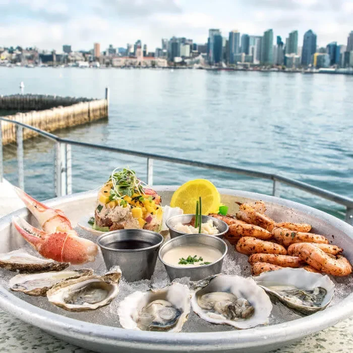 Platter of oysters, shrimp, crab, and ceviche overlooking a city bay.
