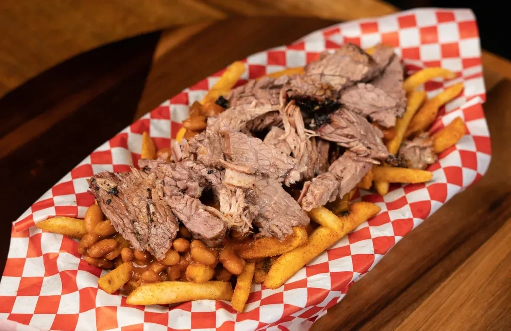 Seasoned fries, baked beans, and pulled pork in a paper boat.