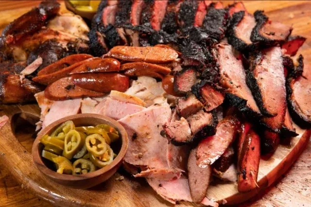 Rustic board with smoked brisket, chicken, sausages, and pickled jalapeños.