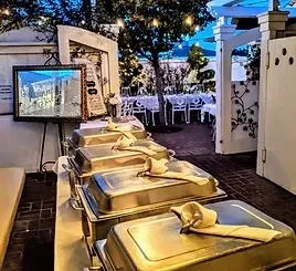 Four chafing dishes at an outdoor evening event with string lights.