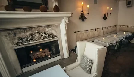 Elegant restaurant interior with ornate fireplace, armchair, and banquette seating.