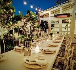 Outdoor dining table set for dinner with candles and string lights.