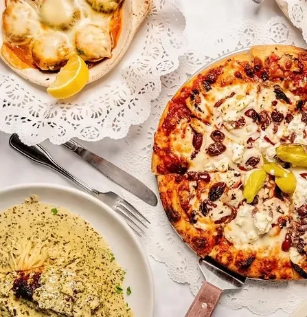 Overhead view of a food spread with pizza, pasta, baked shells.