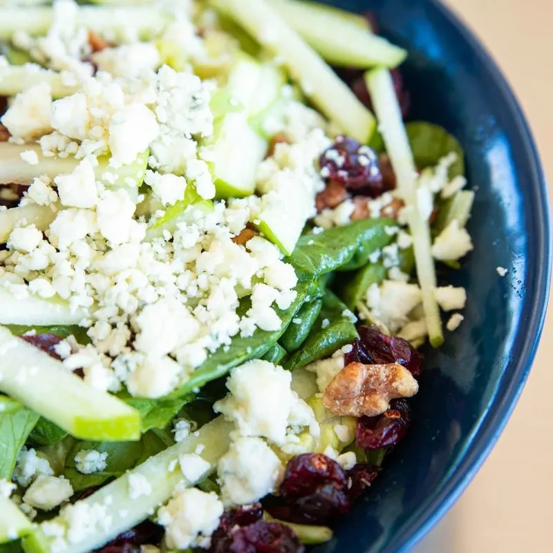 Salad in blue bowl with greens, cheese, apple, cranberries, walnuts.